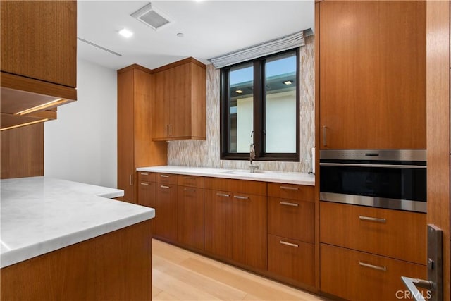 kitchen featuring light countertops, visible vents, brown cabinetry, a sink, and oven