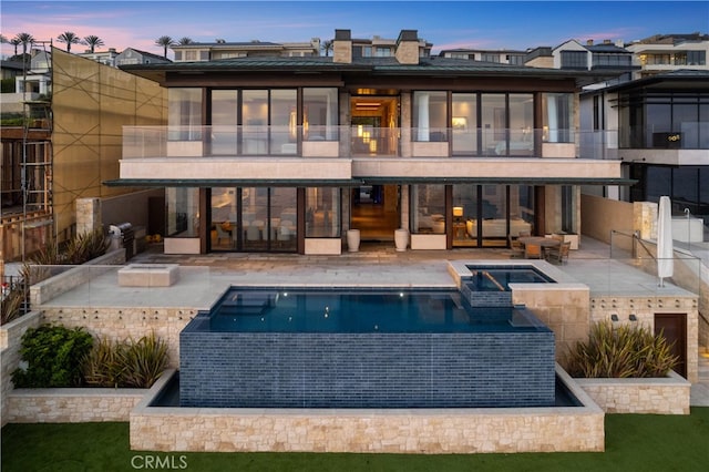 rear view of house featuring a balcony, a patio area, and a pool with connected hot tub