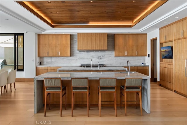 kitchen with a sink, wooden ceiling, a raised ceiling, and a kitchen bar