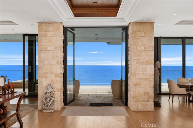 doorway with a water view, expansive windows, a tray ceiling, and wood finished floors