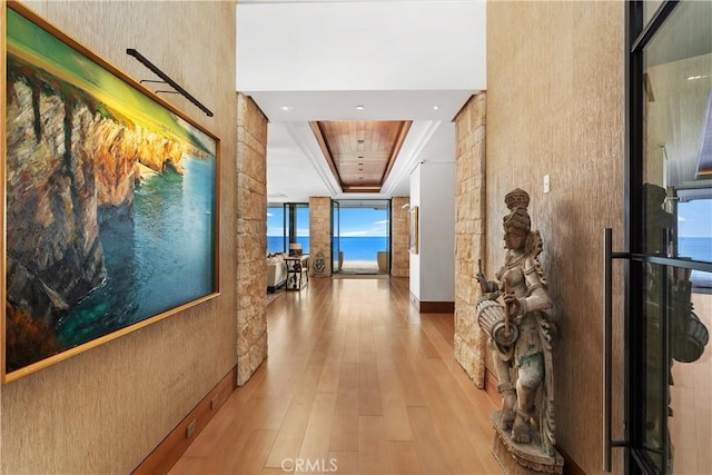 hallway with a raised ceiling, wood finished floors, and a wall of windows