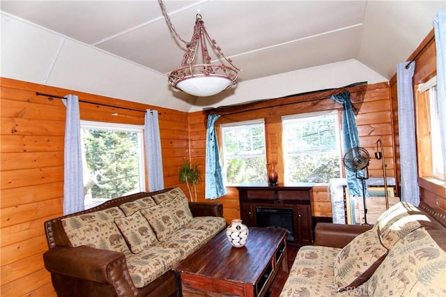 living area featuring lofted ceiling, a glass covered fireplace, plenty of natural light, and wood walls