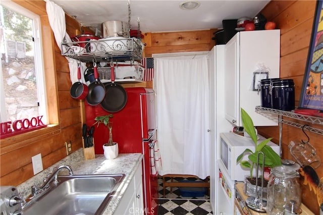 kitchen with white microwave, wooden walls, a sink, white cabinetry, and tile patterned floors