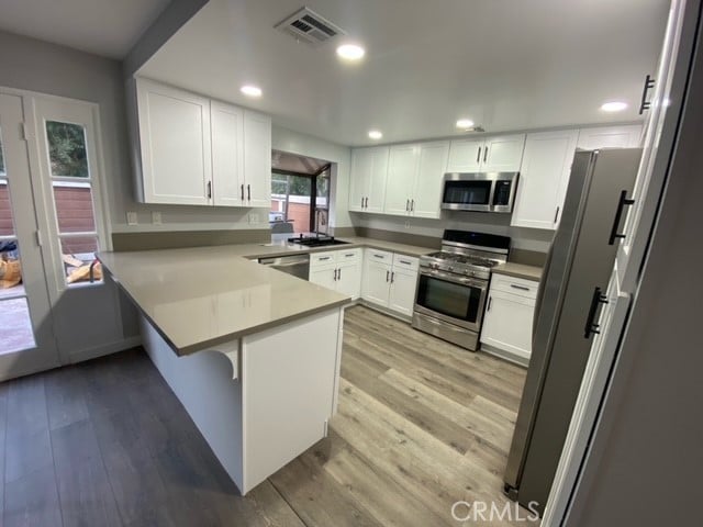 kitchen featuring white cabinets, appliances with stainless steel finishes, kitchen peninsula, and light hardwood / wood-style flooring