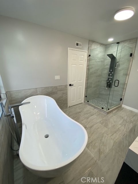 bathroom with shower with separate bathtub and tile walls