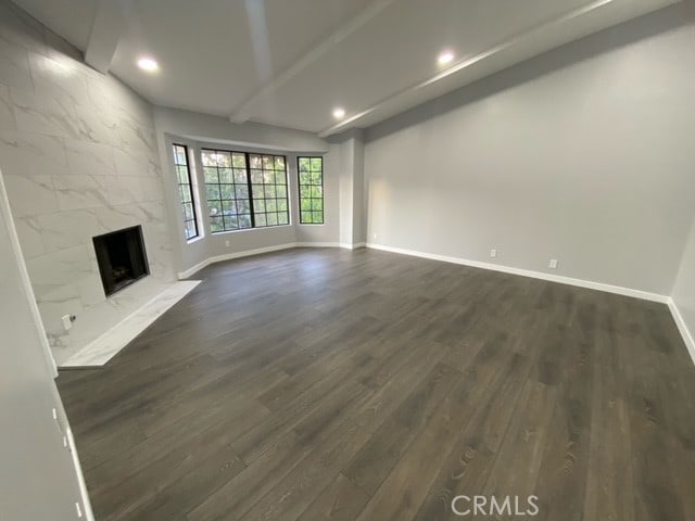 unfurnished living room with a fireplace, lofted ceiling with beams, and dark hardwood / wood-style flooring