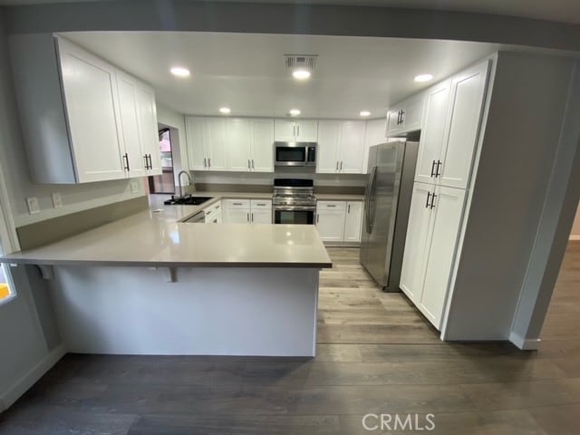 kitchen featuring white cabinets, hardwood / wood-style flooring, sink, kitchen peninsula, and appliances with stainless steel finishes