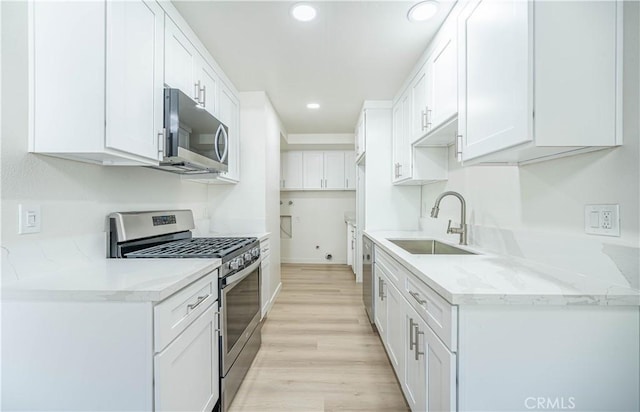 kitchen featuring light stone countertops, appliances with stainless steel finishes, sink, light hardwood / wood-style flooring, and white cabinets