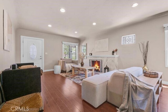 living room with recessed lighting, baseboards, a lit fireplace, and wood finished floors