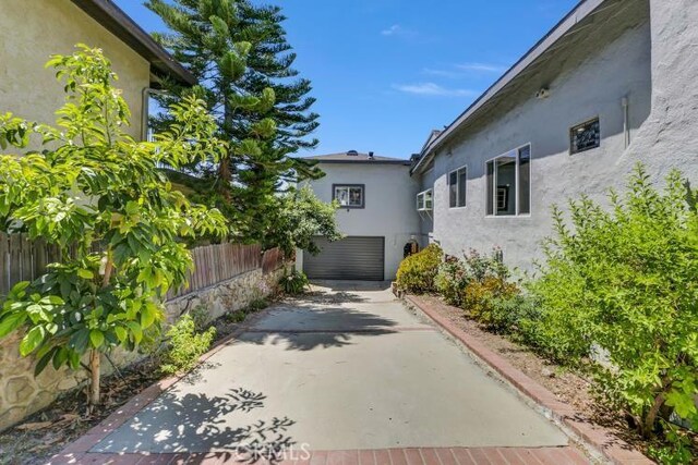 view of property exterior featuring stucco siding, driveway, an attached garage, and fence