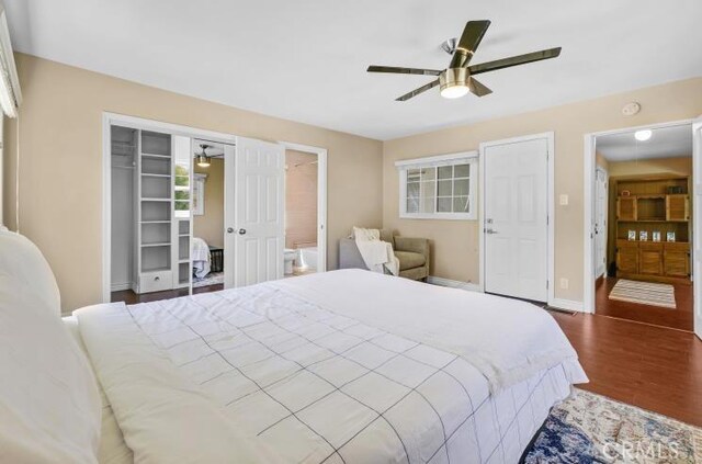 bedroom with ceiling fan, baseboards, ensuite bathroom, a closet, and dark wood-style flooring