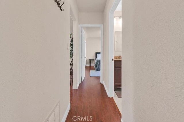 corridor featuring visible vents, dark wood-type flooring, baseboards, and a textured wall