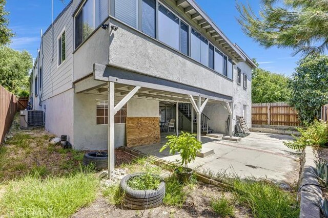 rear view of house with stucco siding, a patio, fence, cooling unit, and stairs