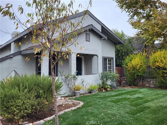 view of side of property with stucco siding, a lawn, and fence