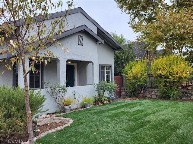 view of home's exterior featuring a lawn, fence, and stucco siding