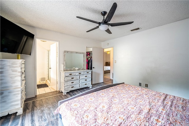 bedroom with a spacious closet, dark wood-type flooring, a closet, a textured ceiling, and ceiling fan