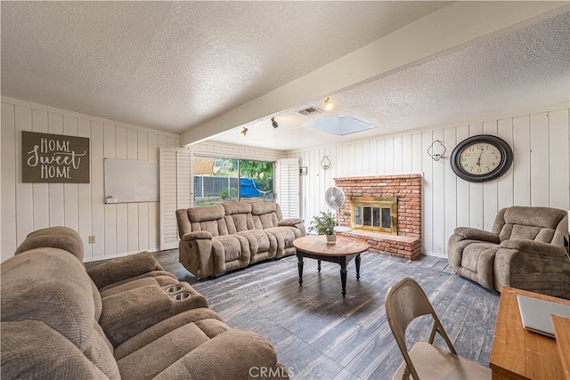 living room with a brick fireplace, a textured ceiling, hardwood / wood-style floors, and wooden walls