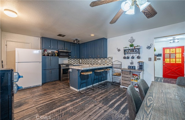 kitchen with kitchen peninsula, tasteful backsplash, blue cabinetry, appliances with stainless steel finishes, and a breakfast bar area