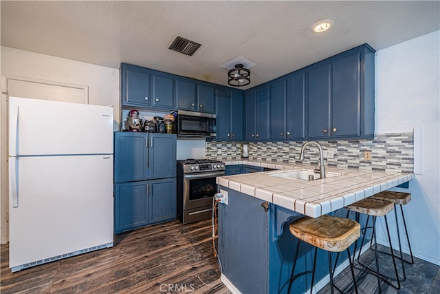 kitchen with appliances with stainless steel finishes, tile counters, blue cabinets, and sink