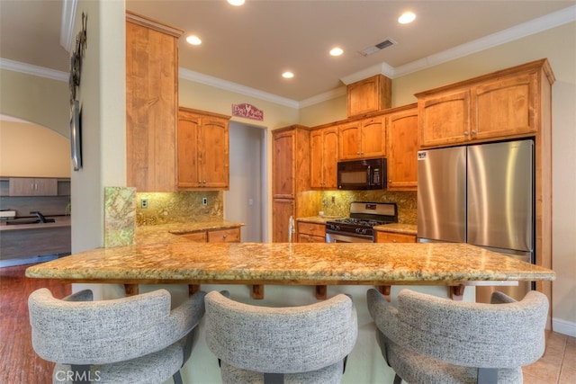 kitchen featuring backsplash, kitchen peninsula, a kitchen bar, and stainless steel appliances