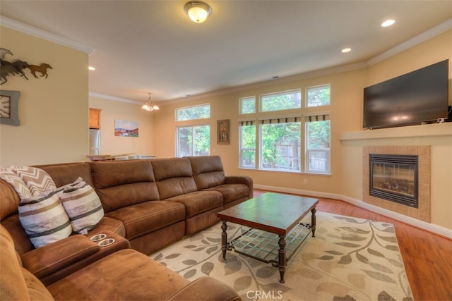 living room with an inviting chandelier, crown molding, a tiled fireplace, and light hardwood / wood-style flooring