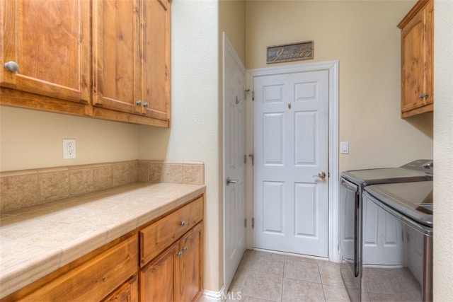 clothes washing area featuring separate washer and dryer, light tile patterned floors, and cabinets