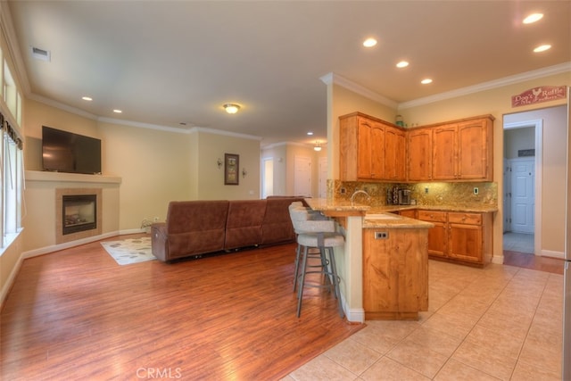 kitchen with a breakfast bar, kitchen peninsula, light hardwood / wood-style flooring, backsplash, and crown molding