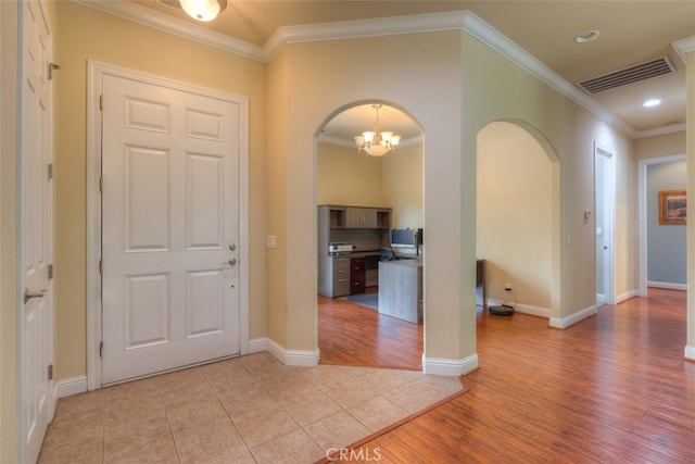 foyer entrance with light wood-type flooring, ornamental molding, and a notable chandelier