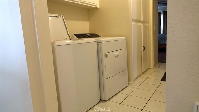 clothes washing area with cabinets, washer and clothes dryer, and light tile patterned floors