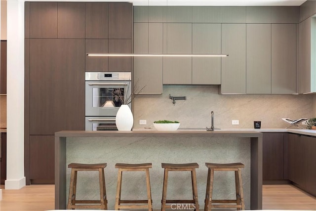 kitchen featuring a kitchen breakfast bar, light hardwood / wood-style floors, double oven, and tasteful backsplash