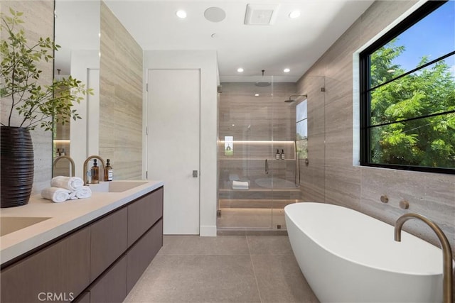 bathroom with tile patterned floors, vanity, independent shower and bath, and tile walls