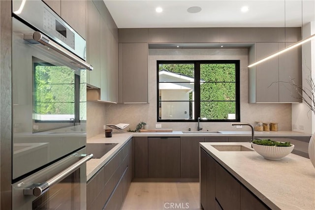 kitchen with black electric stovetop, sink, stainless steel double oven, and light wood-type flooring