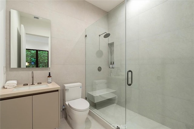 bathroom featuring tile patterned flooring, an enclosed shower, toilet, vanity, and tile walls