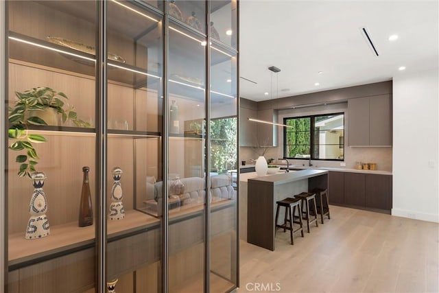 kitchen featuring backsplash, a kitchen island, decorative light fixtures, light hardwood / wood-style floors, and a kitchen bar