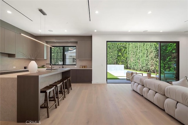 kitchen with sink, hanging light fixtures, a kitchen breakfast bar, light hardwood / wood-style flooring, and backsplash