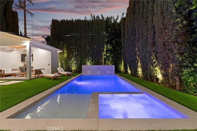 pool at dusk featuring outdoor lounge area, a patio, and a lawn