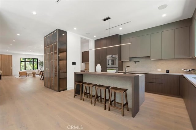 kitchen featuring tasteful backsplash, light hardwood / wood-style flooring, a breakfast bar area, and stainless steel double oven