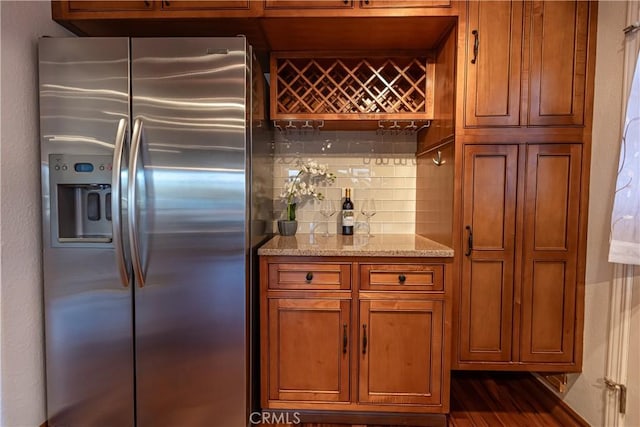 bar with dark hardwood / wood-style flooring, light stone countertops, stainless steel fridge, and backsplash