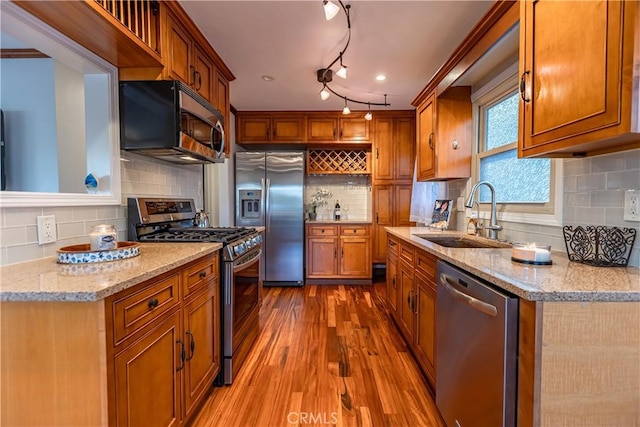 kitchen with sink, stainless steel appliances, tasteful backsplash, wood-type flooring, and light stone countertops