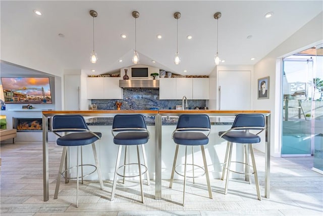 kitchen featuring decorative light fixtures, a breakfast bar area, decorative backsplash, and white cabinets