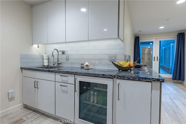 kitchen with white cabinets, light hardwood / wood-style flooring, wine cooler, and decorative backsplash