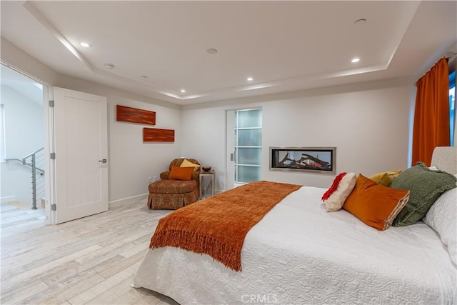 bedroom with light wood-type flooring and a tray ceiling