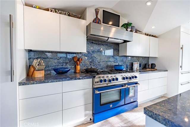 kitchen with range with two ovens, ventilation hood, white cabinets, and backsplash