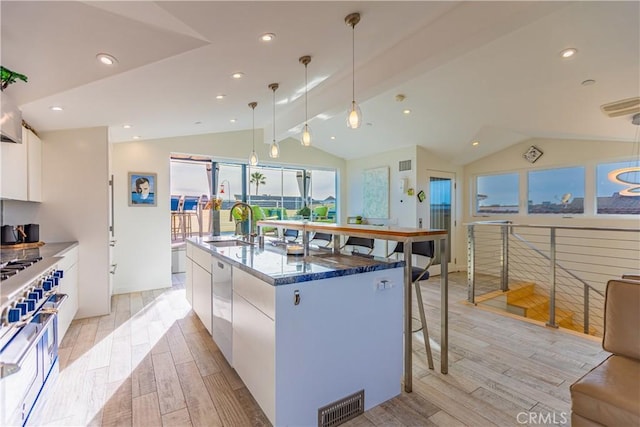 kitchen with white cabinetry, vaulted ceiling, hanging light fixtures, dark stone counters, and a kitchen island with sink