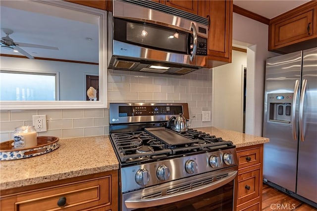 kitchen featuring backsplash, ornamental molding, light stone countertops, and appliances with stainless steel finishes