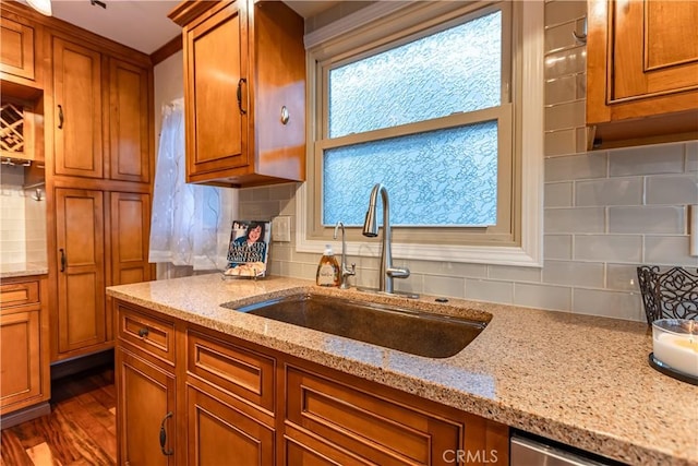 kitchen with dark wood-type flooring, sink, dishwasher, light stone countertops, and decorative backsplash