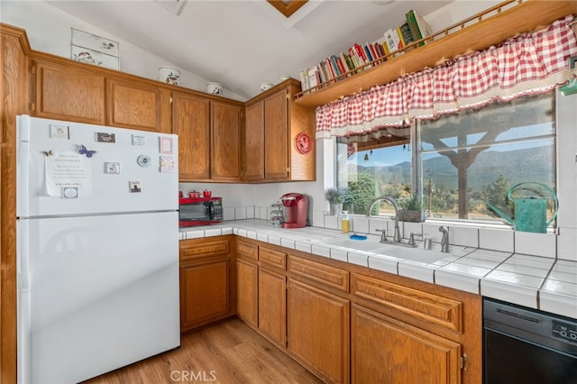 kitchen with sink, vaulted ceiling, white refrigerator, tile countertops, and light wood-type flooring