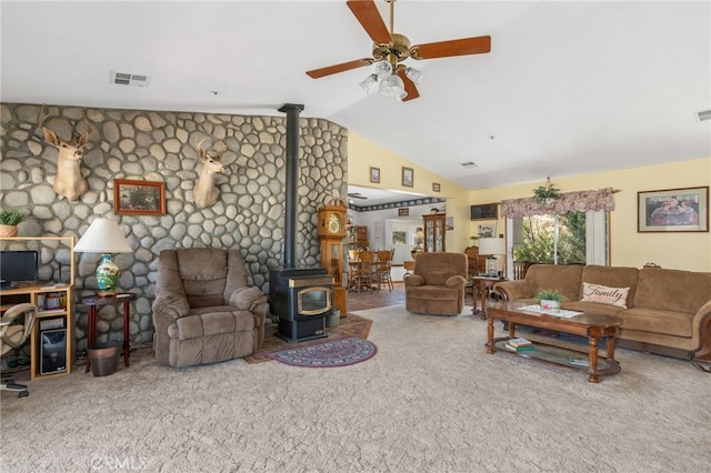 carpeted living room featuring vaulted ceiling, ceiling fan, and a wood stove