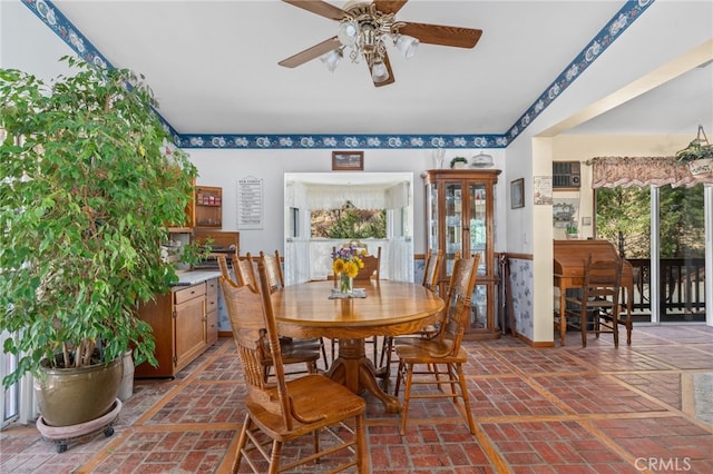 dining space featuring brick floor, a ceiling fan, and baseboards