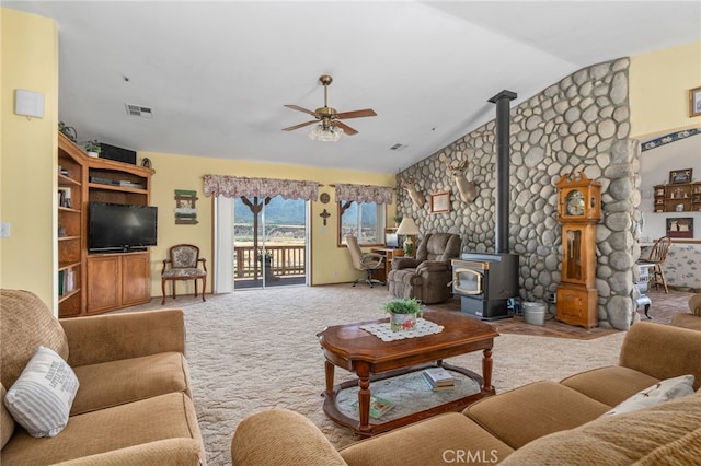 carpeted living area featuring lofted ceiling, a wood stove, a ceiling fan, and visible vents